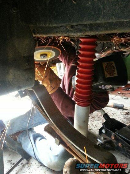 Person grinding on vehicle frame with sparks flying; red shock absorber visible