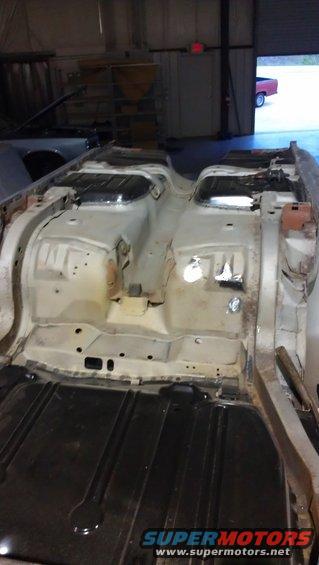 Car floor pan stripped down for restoration, showing structural components and seat mounts