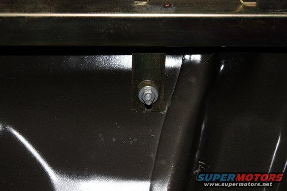 Close-up of a metal bracket with a bolt and washer attached to a dark surface inside a vehicle
