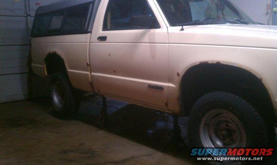 Cream-colored pickup truck with a camper shell, showing rust spots and a side view