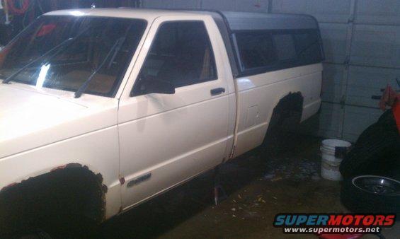 1991 Chevrolet S10 pickup truck with a black camper shell, showing rust on wheel wells