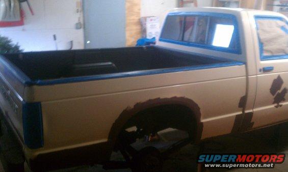 Pickup truck with rust around wheel well, taped for painting. Beige body, dark bed