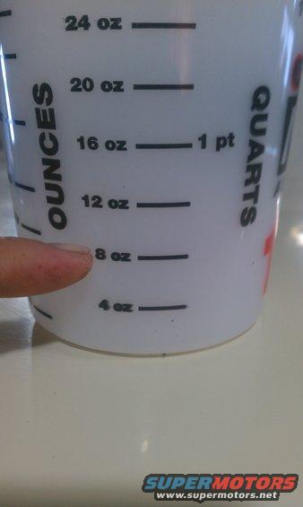 Finger pointing to the 8 oz mark on a measuring cup with ounce and quart markings