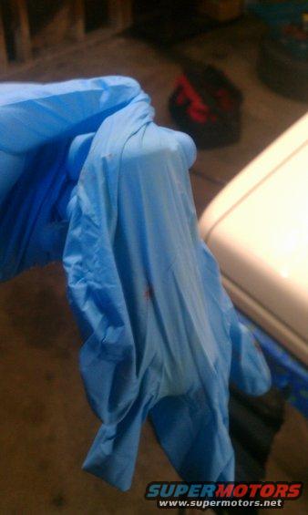 Blue nitrile glove with red stains, held in a gloved hand
