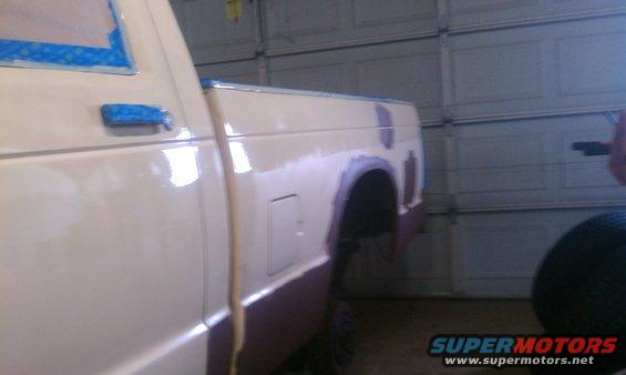 White pickup truck bed and rear quarter panel with body filler and primer, taped windows, in a garage