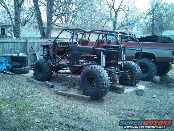 Off-road buggy with roll cage and large tires, partially disassembled, next to a red pickup truck