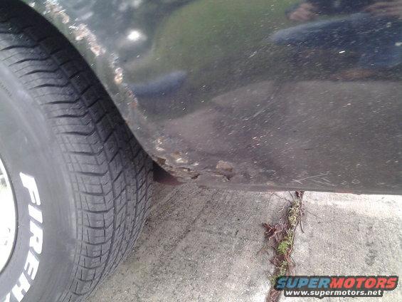 Close-up of a car's rear fender showing rust and a Firestone tire