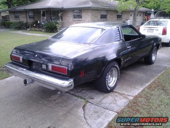 Black 1975 Chevrolet Chevelle coupe parked on driveway, rear 3/4 view. Chrome bumper, louvers on rear window
