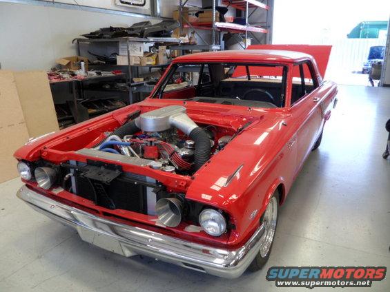 Red custom coupe with engine exposed, hood and trunk open, in a workshop
