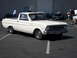 1973 Ford Ranchero - A white pickup truck is parked in a lot with other vehicles and people around.
