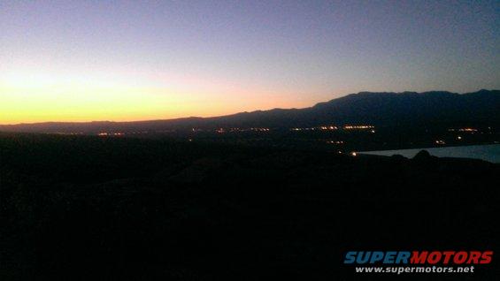 Sunset over a valley with distant city lights and mountains
