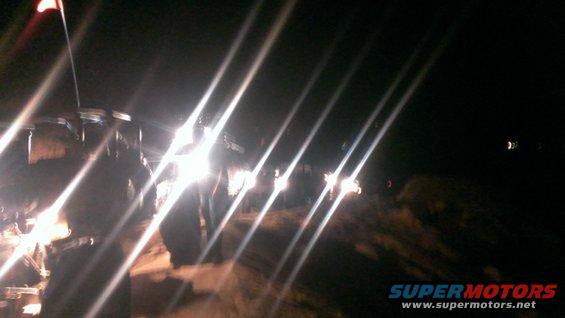 Multiple off-road vehicles with bright headlights on a dirt path at night