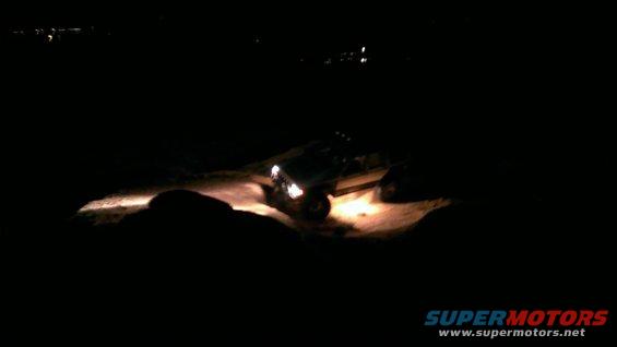 Off-road vehicle driving on dirt at night with headlights on