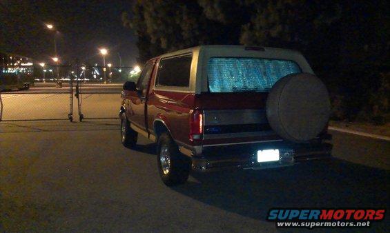 Red Ford Bronco parked at night, rear view showing spare tire on tailgate and reflective window cover