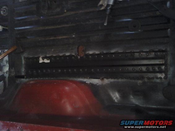 Interior floor pan with red wheel well, black ribbed metal, and visible rivets