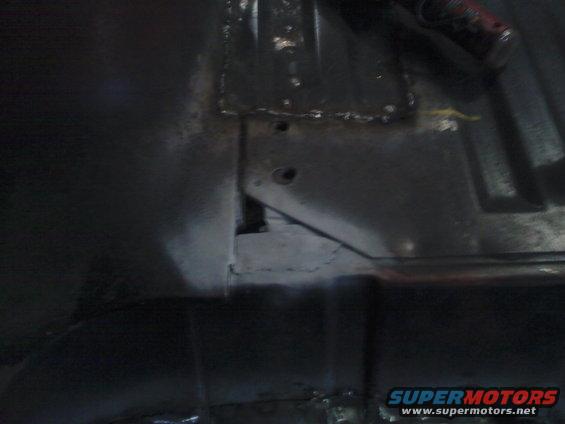 close-up of a dark, possibly rusty, vehicle undercarriage with some metal bracing and holes