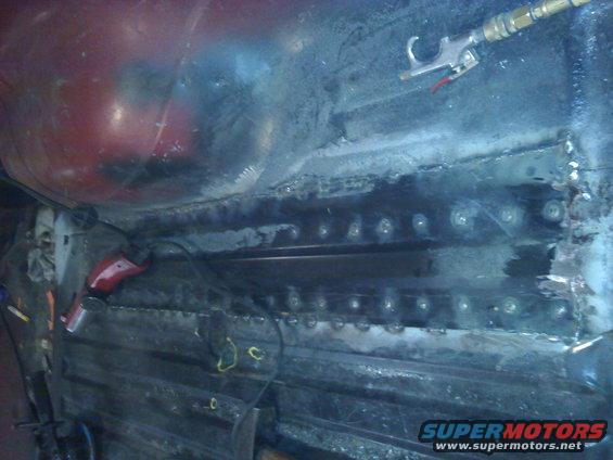 Close-up of vehicle floor pan with welding repairs and an air blow gun