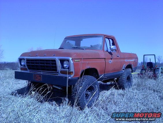 Red 1978 Ford Bronco parked in a grassy field with a tractor in the background