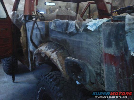 Side view of a rusty Ford Bronco undergoing restoration, with doors open and interior covered