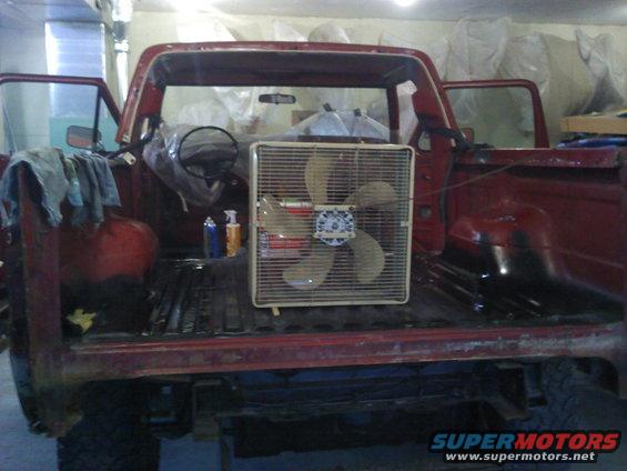 1978 Ford Bronco with doors open, a box fan in the bed, and items on the driver's side