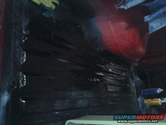 Looking into the dark interior of a vehicle, possibly a truck bed or cargo area, with some red paint visible on the upper right