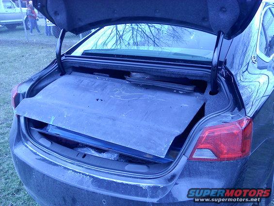 Car trunk open, showing a blue mat and some items underneath. Rear taillight visible on the right