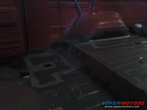 Red vehicle interior floor with gray sealant applied to sections. A black can sits on the left