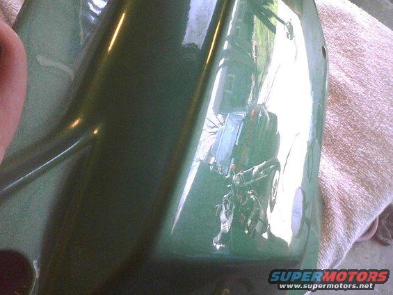 Reflection in a green car part shows a motorcycle and a house