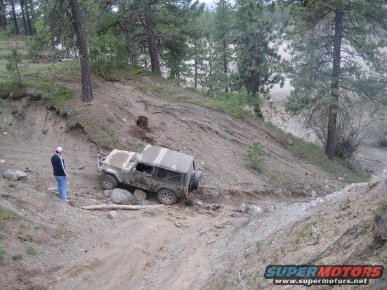 Tan 2005 Jeep Wrangler navigating a steep, rocky dirt trail with a person standing nearby