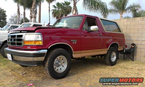Red 1994 Ford Bronco 3/4 front view with tan trim. Another white vehicle is partially visible