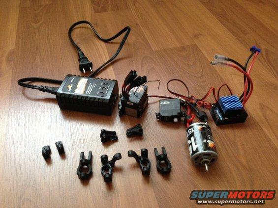 RC car charger, motor, servos, and suspension parts on wooden floor