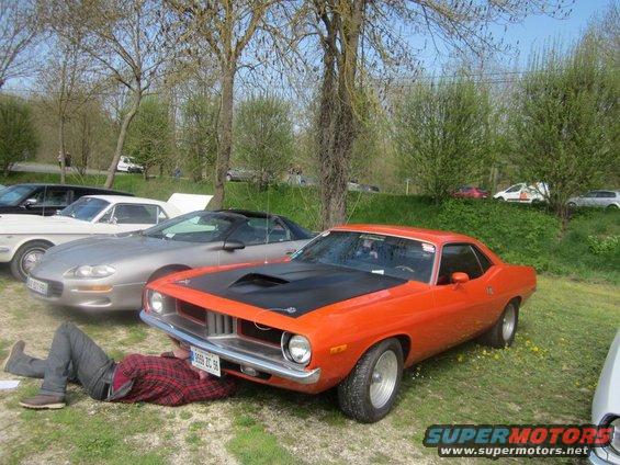 Guy working under an orange muscle car, another car next to it