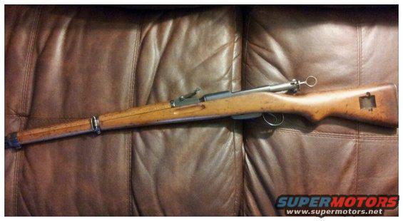 Bolt-action rifle with wooden stock and metal barrel, resting on a brown leather surface