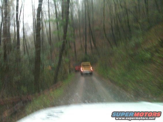 Yellow SUV and another vehicle driving on a wet dirt road through a forest