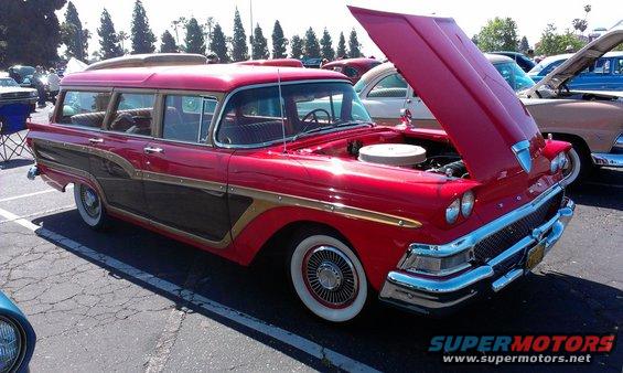 Red station wagon with wood paneling, hood open, parked at an outdoor car show. Another car is visible behind it