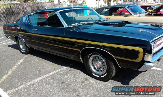 Black 1970 Ford Torino GT coupe with gold side stripes and hood scoop, parked in a lot