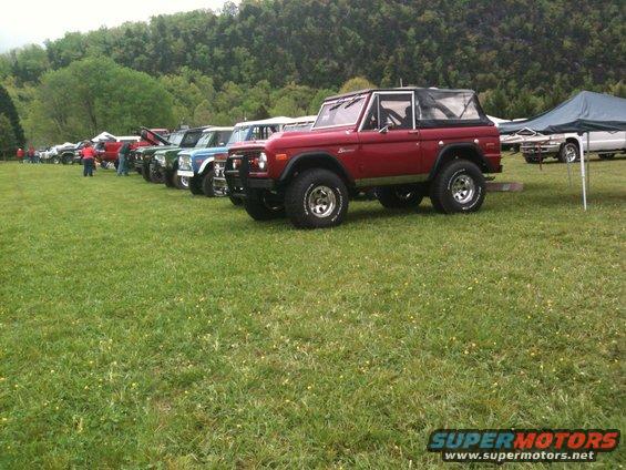 Red 1978 Ford Bronco parked in a line with other Broncos on a grassy field