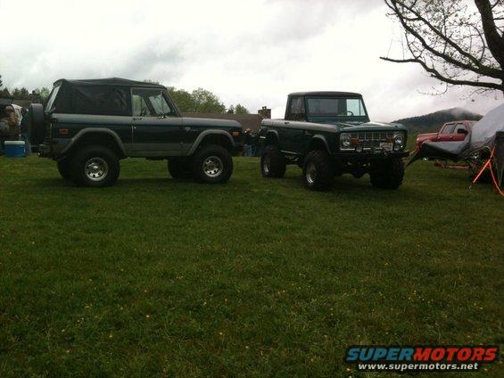 Two dark green Ford Broncos parked on grass, one with a soft top, the other a pickup
