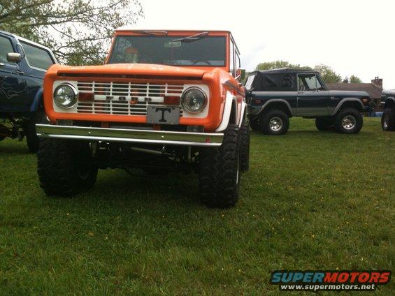 Orange Ford Bronco with lifted suspension and large tires, parked on grass next to another Bronco
