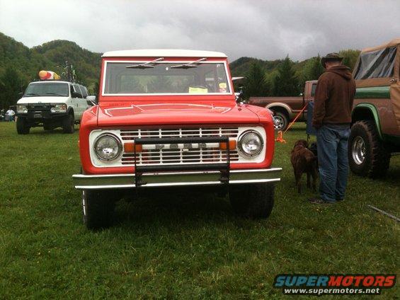 Red Ford Bronco with white top, front view, parked on grass with other vehicles