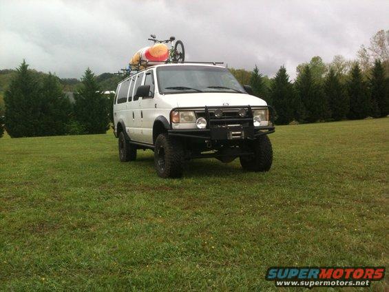 White van with kayak and bicycle on roof rack, lifted suspension, and bull bar