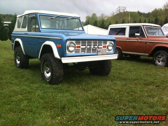 Blue Ford Bronco with white top and chrome wheels, parked on grass