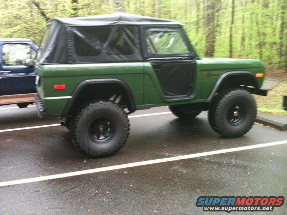 Green first-generation Ford Bronco with soft top parked next to a blue truck