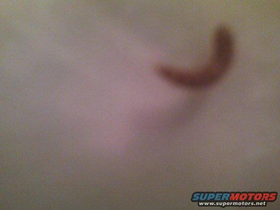 Blurry brown curved object on a light-colored surface, possibly a car interior part. Text 'SUPERMOTORS' is visible