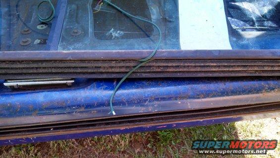 Close-up of a blue vehicle's door frame showing a rubber seal and some green wiring. The area appears worn