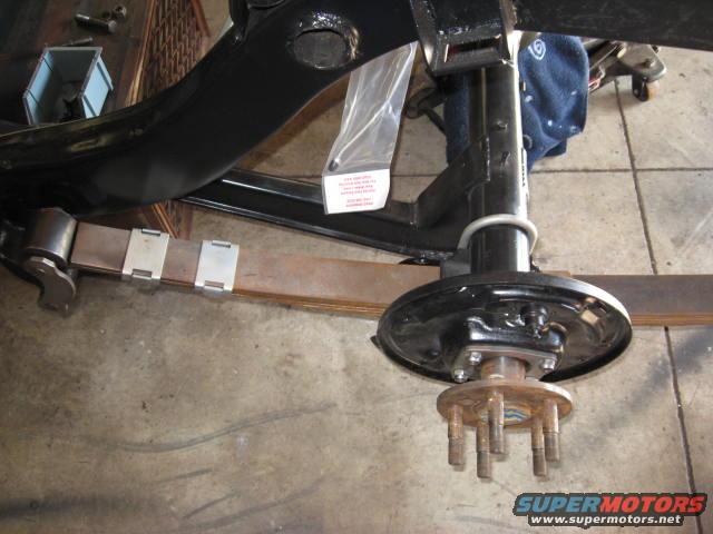 Rear axle assembly with leaf spring and brake drum. A plastic bag with instructions is attached to the frame