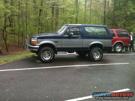 Side view of a 1992 Ford Bronco in blue and silver parked next to a red SUV