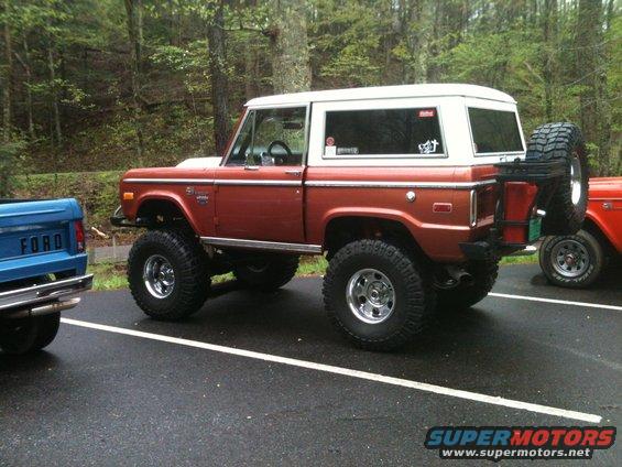 Orange Ford Bronco with lifted suspension and spare tire on rear, parked next to a blue Ford pickup truck