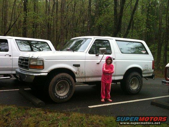 1992 Ford Bronco parked next to another white SUV, with a child in pink standing beside it