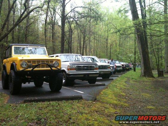 Yellow Ford Bronco with aftermarket bumper and large tires parked in a line of trucks